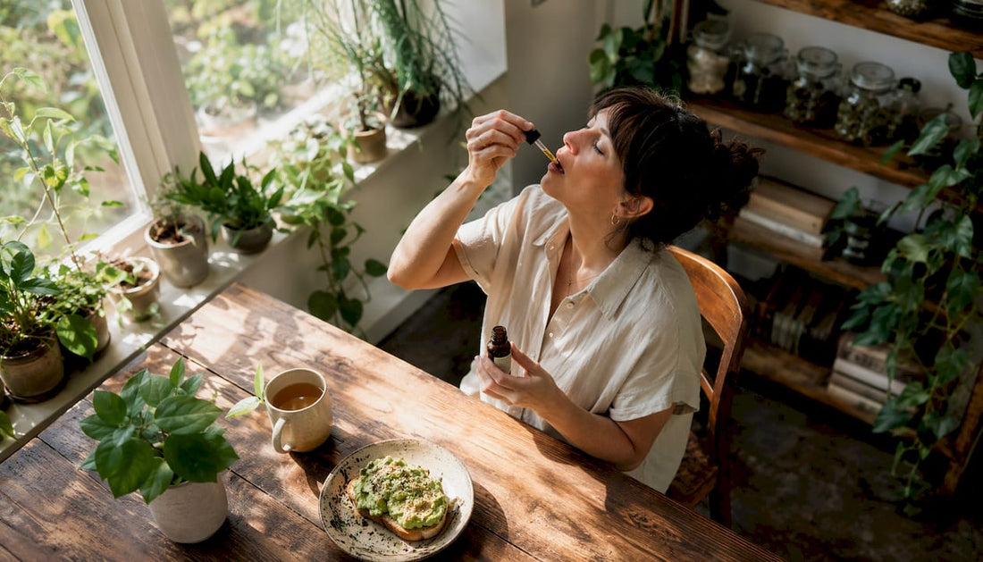 Woman taking CBD drops under tongue at kitchen table
