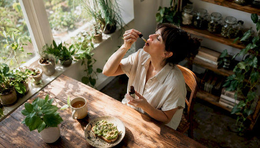 Woman taking CBD drops under tongue at kitchen table